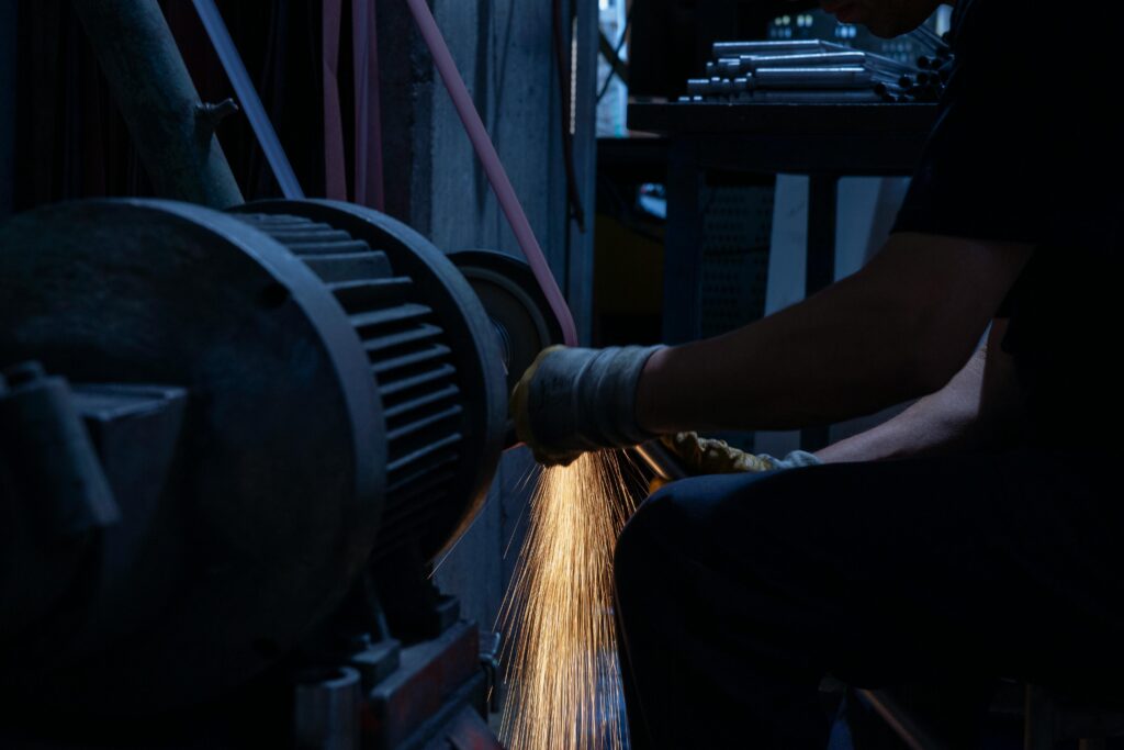 A worker in a factory uses a grinding machine, generating bright sparks in a dark industrial setting.